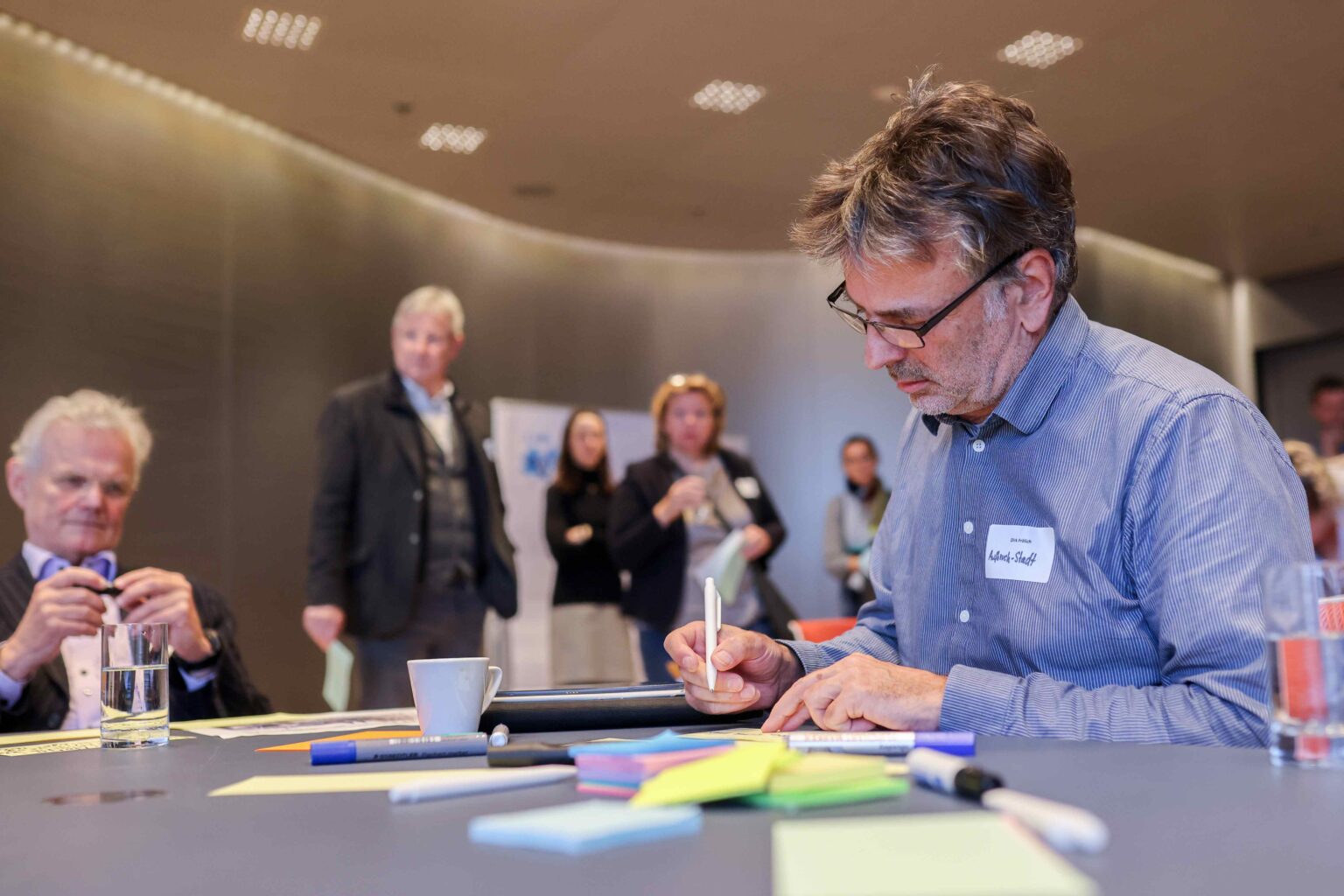 Ein Mann schreibt auf einem Blatt Papier bei einer Konferenz.