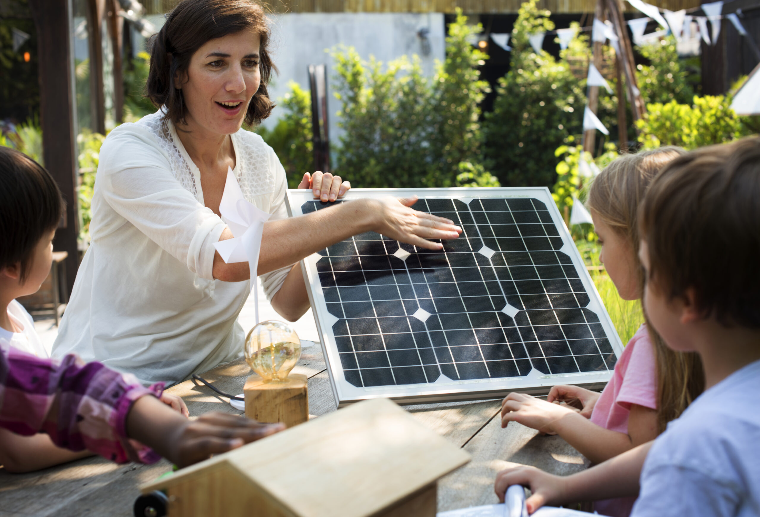 Frau zeigt Kindern den Umgang mit einem Solarpanel.